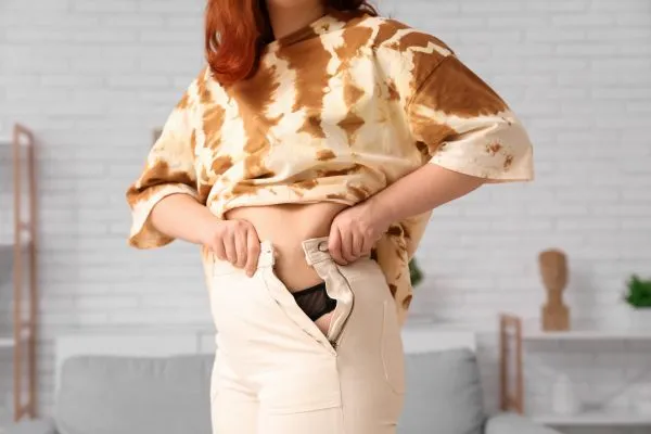 Image of woman trying to do her trousers up after pregnancy weight gain Eynsham