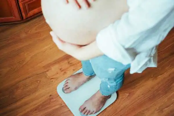 Image of woman weighing herself and experiencing weight gain through pregnancy Eynsham